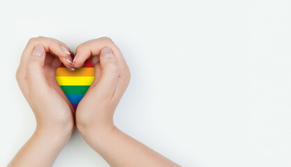 Female hand holding heart with LGBT flag on white background.