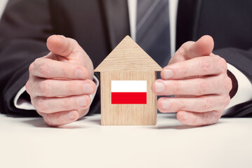 Businessman hand holding wooden home model with Polish flag. insurance and property concepts