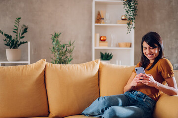 Beautiful woman using smartphone while relaxing on the sofa at home