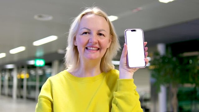 satisfied happy middle aged blonde woman showing thumb up holding phone with white screen in airport train station in office advertisement smile joy space for text woman phone advertise study tickets