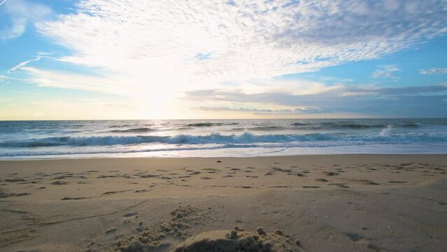 Low-angle shot of sea waves flooding the sandy sunlit Bethany beach at sunset skyline background