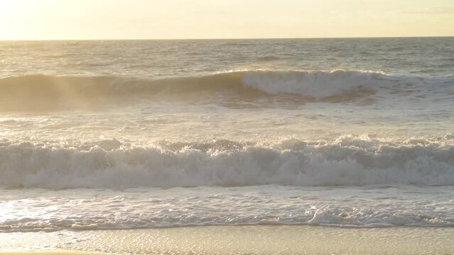 Closeup shot of sea waves flooding the sandy sunlit Bethany beach at sunset skyline background