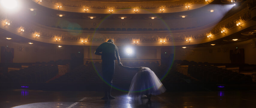 Ballet dancers bow at the end of choreography rehearsal on classic theater stage illuminated by spotlight. Dance partners prepare for theatrical dance performance. Art of classical ballet dance.