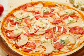 Freshly baked pizza with smoked chicken fillet and gorgonzola cheese served on wooden background with tomatoes, sauce and herbs. Food delivery concept. Restaurant menu