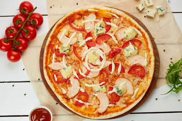 Freshly baked pizza with smoked chicken fillet and gorgonzola cheese served on wooden background with tomatoes, sauce and herbs. Food delivery concept. Restaurant menu. Top view