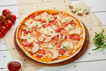 Freshly baked pizza with smoked chicken fillet and gorgonzola cheese served on wooden background with tomatoes, sauce and herbs. Food delivery concept. Restaurant menu
