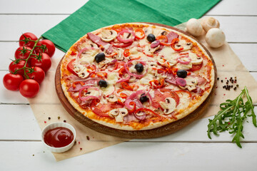 Freshly baked pizza with smoked sausages, red pepper, mushrooms, onion and olives served on wooden background with tomatoes, sauce and herbs. Food delivery concept. Restaurant menu