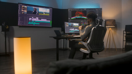 African American multimedia artist drinks coffee and makes color grading in editing program on...