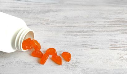 orange jelly candies such as orange slices, vitamins scattered from a jar isolated on a wooden...