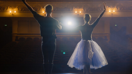 Ballet dancers bowing during choreography rehearsal on classic theater stage illuminated by...