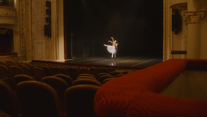 Establishing shot of ballet dancers practicing choreography on classic theater stage. Man and woman prepare theatrical performance. Shooting from spectator seat. Dramatic lighting. Full shot of stage.