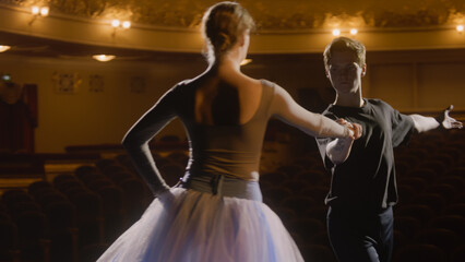 Elegant ballet dancers perform ballet movements on theater stage during choreography rehearsal. Man and woman practice and prepare for dance performance. Classical ballet dance art. Dramatic lighting.