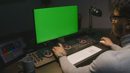 African American film maker works on computer in studio with digital equipment. Color grading...