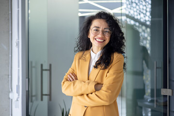 Portrait of successful business woman inside office, latin american boss in yellow suit smiling and...