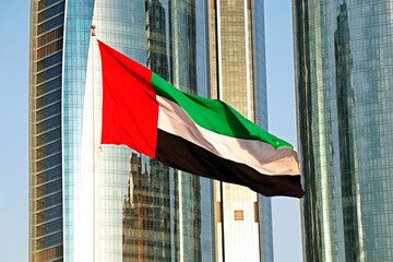 united arab emirates (uae) national flag waves on air in the sky in front of tall buildings in abu dhabi