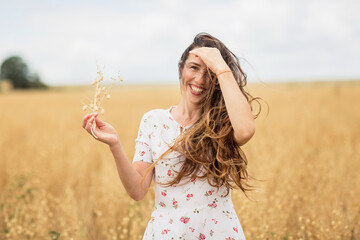 A brunette woman in a white dress runs along a field