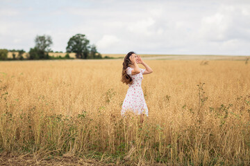 Fototapeta na wymiar A brunette woman in a white dress runs along a field
