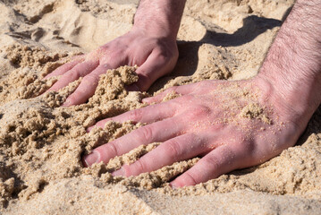 Hands of a man grabbing sand on the beach.