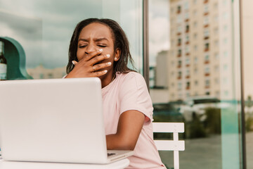 Tired exhausted overworked african american woman hipster sitting outside with laptop yawning. Young entrepreneur freelancer student businesswoman low energy need to sleep have a rest chill