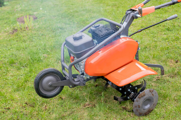Fototapeta premium A man works the land in the garden with a cultivator, prepares the soil for sowing. farming concept.Garden tiller to work, walk-behind tractor.plow the field with a farm tractor