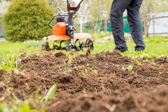 A man works the land in the garden with a cultivator, prepares the soil for sowing. farming concept.Garden tiller to work, walk-behind tractor.plow the field with a farm tractor