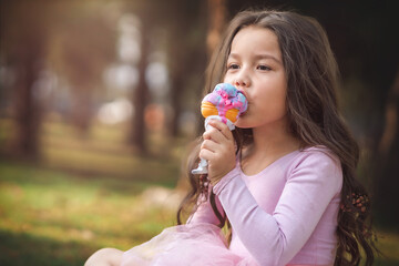 Cute blonde curly-haired girl eating a nice ice cream in the park, concept of children's day, copy space