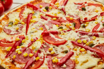 Freshly baked tasty pepperoni pizza with salami, mozzarella cheese, corn and pepper served on wooden background with tomatoes, sauce and herbs. Food delivery concept. Restaurant menu