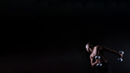 Obraz na płótnie Canvas Isolated african muscular man with dumbbells on dark studio background. Strong shirtless black guy