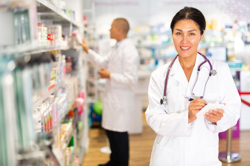 Portrait of an female pharmacist working in pharmacy during the pandemic, standing in trading floor and makes important notes