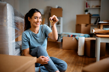 Young happy woman holds key while moving into new home. - obrazy, fototapety, plakaty