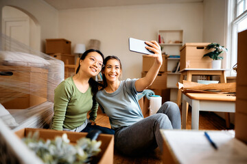 Happy female friends taking selfie after moving into new apartment.