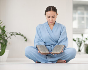 Asian woman sitting in lotus position on yoga mat and holding sadhu boards.