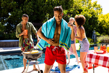Happy diverse group of friends having pool party, barbecuing and dancing in garden