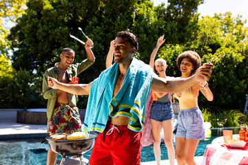 Happy diverse group of friends having pool party, barbecuing and dancing in garden