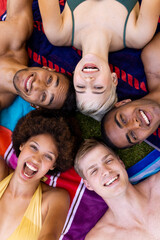 Portrait of happy diverse group of friends lying on towels and smiling in garden