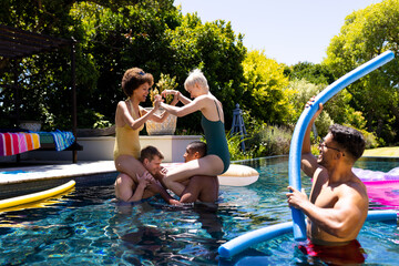 Happy diverse group of friends having pool party, playing in swimming pool in garden