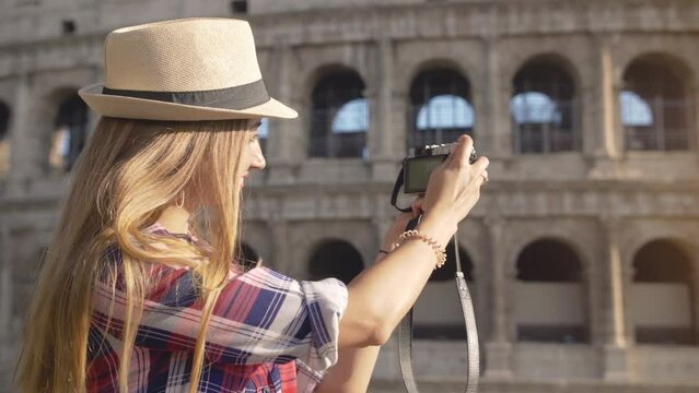 Young blonde woman with blue eyes and long hair, taking pictures with a vintage camera at Colosseum, Rome.
