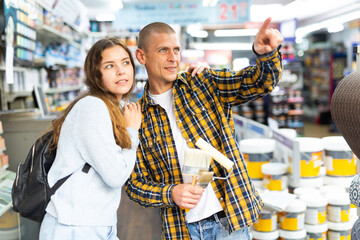 Young cheerful woman and man pointing to shelves at building hypermarket