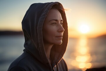 Close up portrait of a beautiful young woman wearing hoodie and looking away while standing on the beach at sunset
