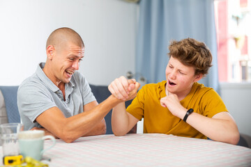 Young boy competing with his father in arm wrestling on kitchen table.