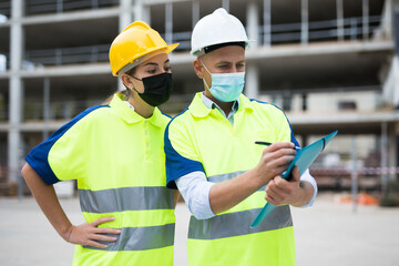 Two builders in uniform and face masks planning their work in construction plant.