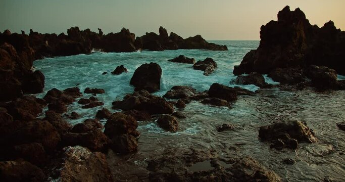 Ocean waves at rocky beach during twilight. Sea water crash and splash on bizzare volcanic rock formations at dusk. Close-up slow-motion.