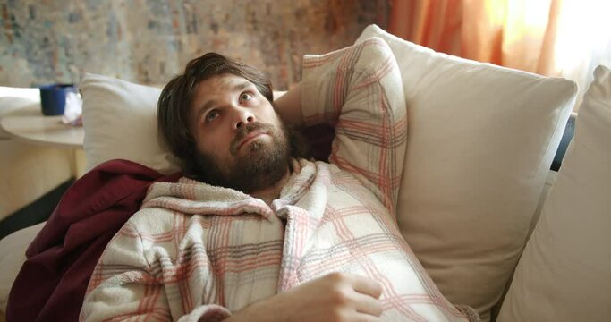 Carefree, careless lazy beard man on the couch staring at the ceiling, looking around out of boredom and idleness. Slacker thinking about procrastination and wasting time. Boredom, laziness concept