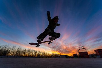 In the evening, a boy is playing skateboard.