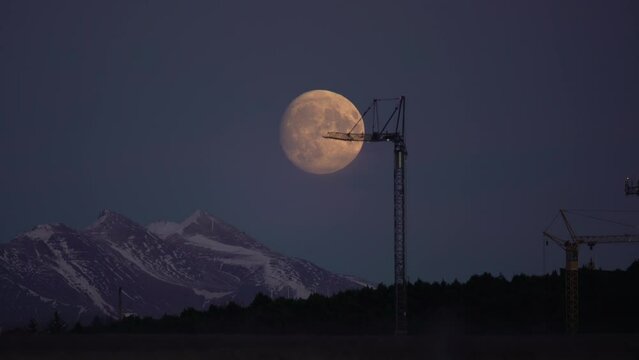 Large full moon rising behind construction crane, Reykjavik Iceland time lapse