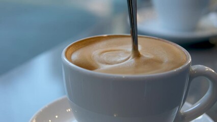very appetizing coffee foam with spoon quickly stir it in white cup background for any advertising screen saver for music latte coffee with milk with cream restaurant blurred background space for ad