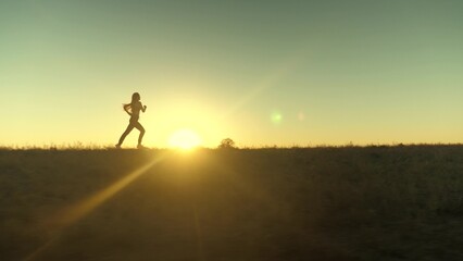 running after sun. training jogging. A healthy beautiful girl is engaged in fitness, jogging in country in sun. Jogger girl breathes fresh air on field. Free young woman runs in summer park at sunset.