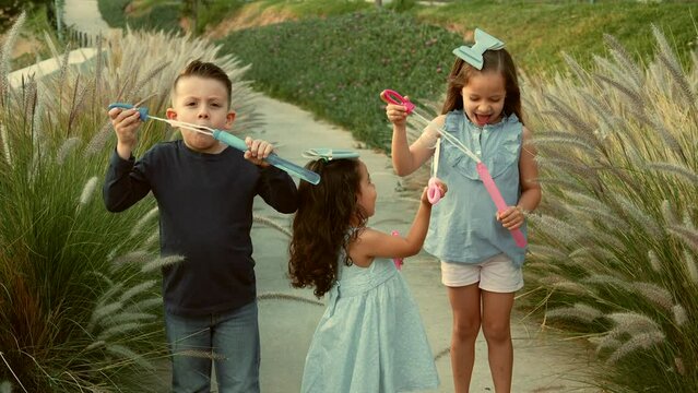 Ni&ntilde;os amigos hermanos jugando y creando burbujas disfrutando sonrientes y divertidos en un dia soleado al atardecer al aire libre en el parque