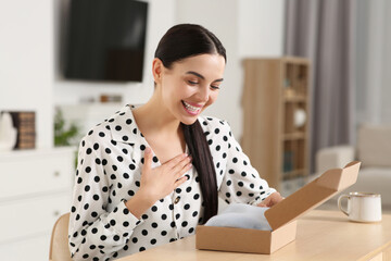 Happy young woman opening parcel at table indoors. Internet shopping