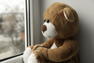 Cute lonely teddy bear on windowsill indoors, closeup. Space for text